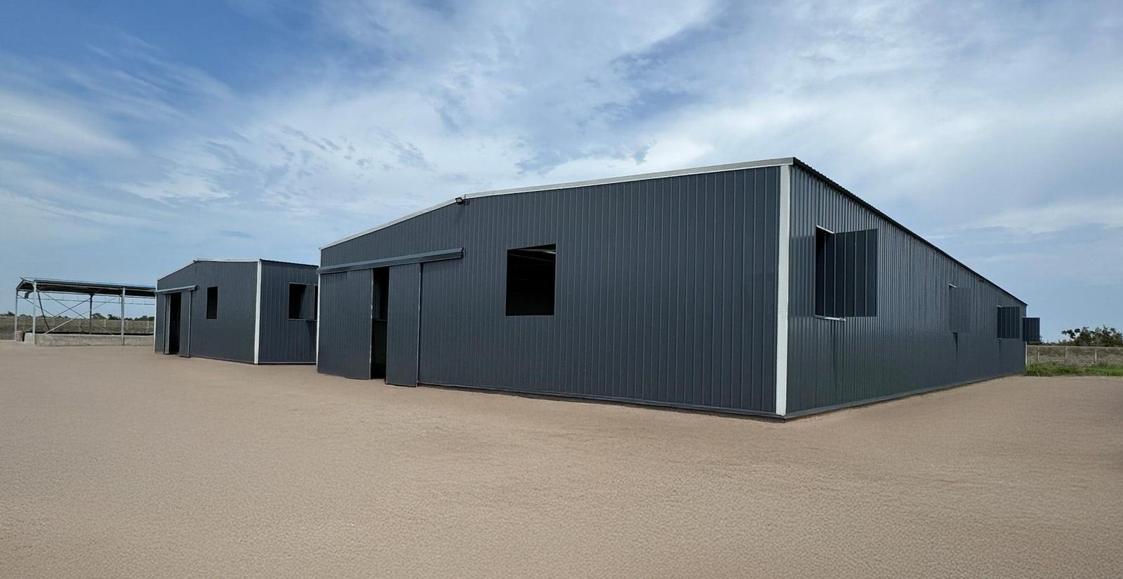 Bâtiment métallique anthracite implanté sur un terrain en terre sous ciel nuageux, Steel Shed for Business