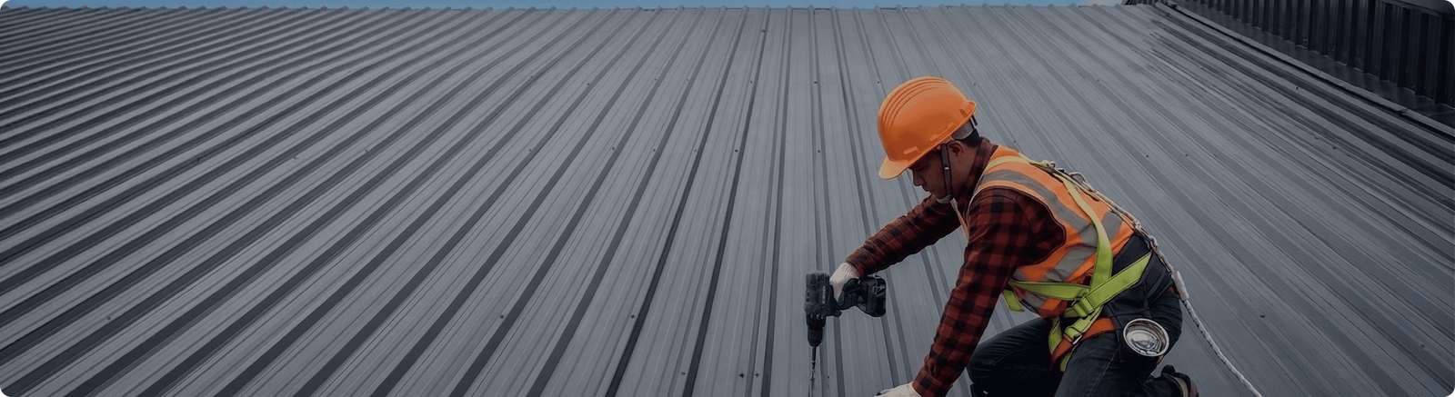 Ouvrier équipé d'un casque et d'un harnais fixant la couverture en bac acier d'un bâtiment métallique, Steel Shed for Business